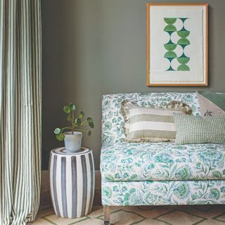 A sage green-painted living room with a floral-print sofa and striped floor-length curtains in green and cream