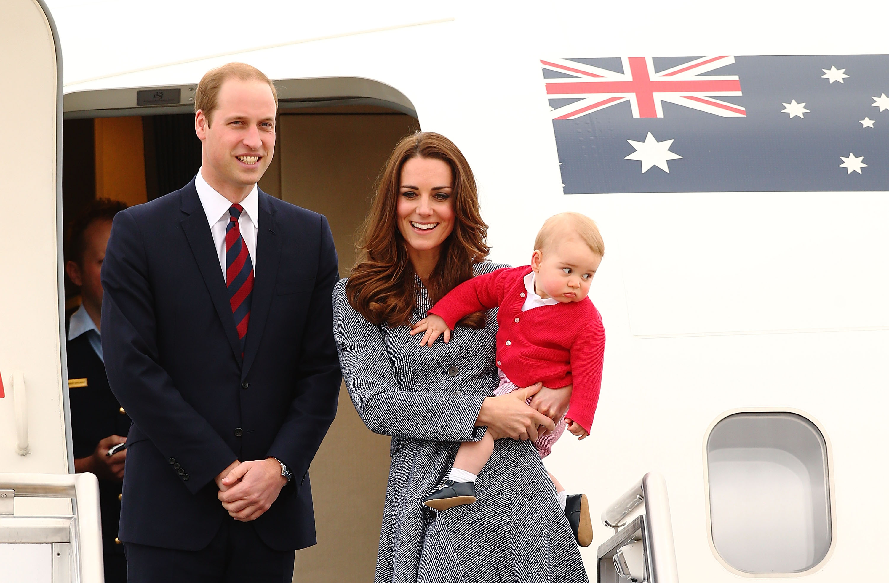 Prince William and Prince George, being held by Princess Kate, exiting a plane with an Australian flag