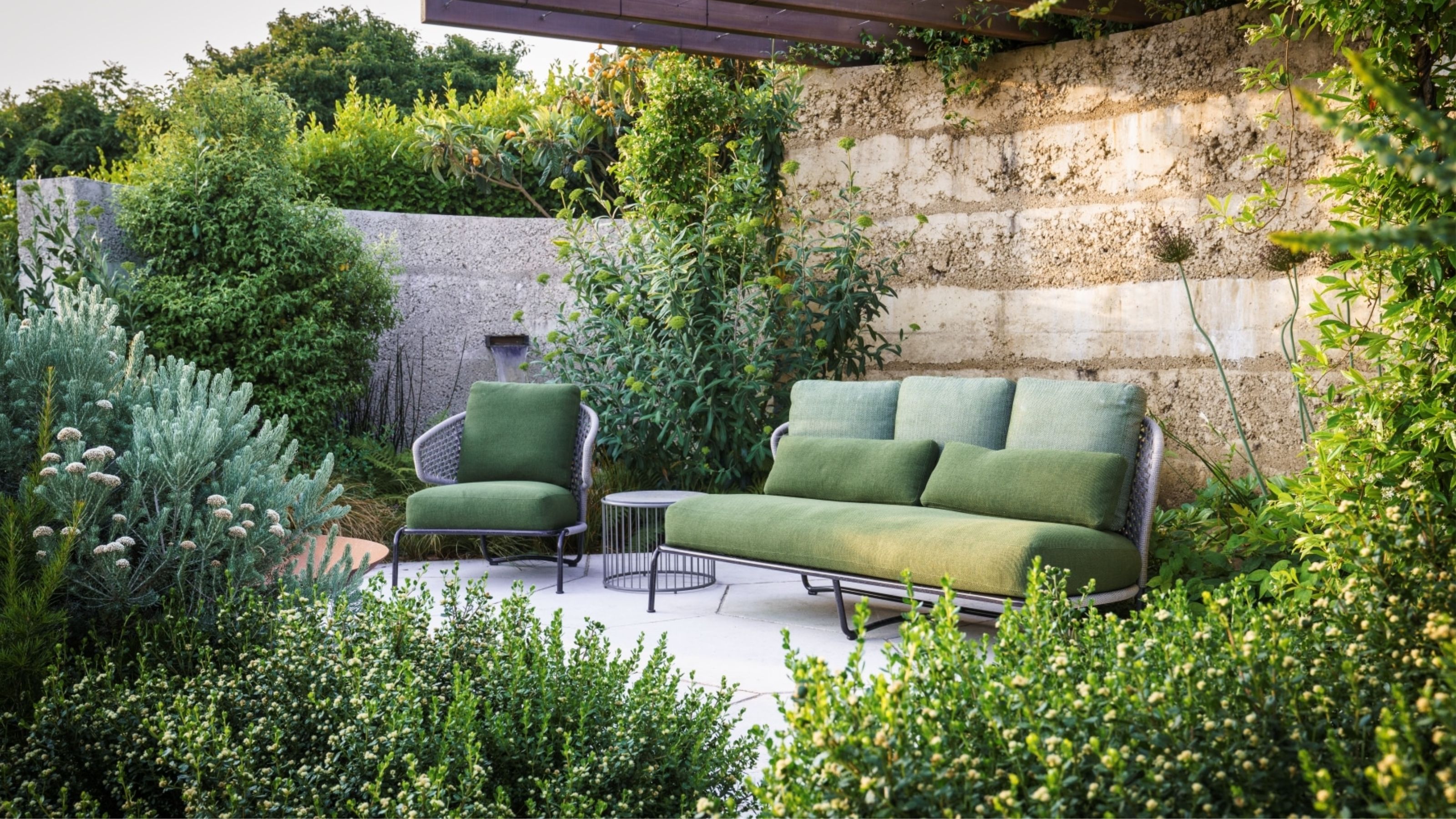 Green outdoor sofa and armchair in a rustic coastal garden with lush planting