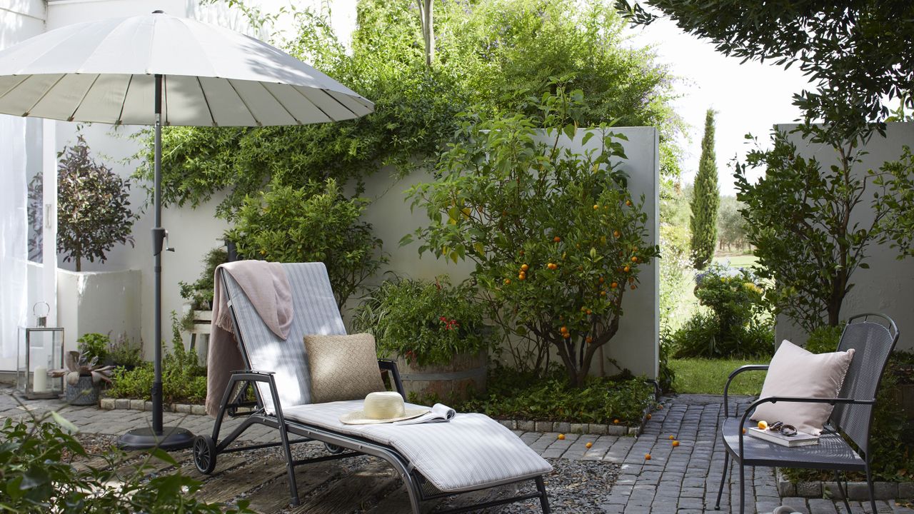 a sun longer, chair and parasol, in a stylish garden with a white brick wall, one of our top tips for how to make a small garden look bigger