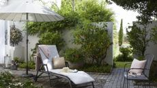 a sun longer, chair and parasol, in a stylish garden with a white brick wall, one of our top tips for how to make a small garden look bigger