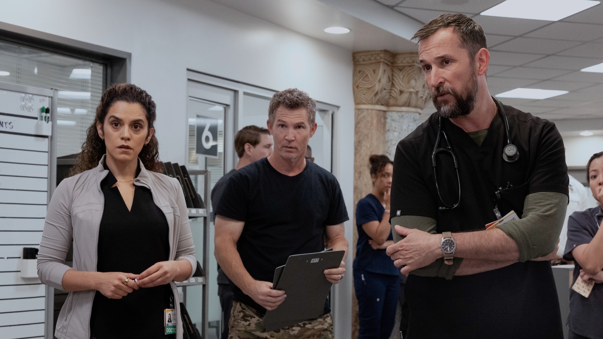 From left to right: Sepideh Moafi, Shawn Hatosy holding a clip board and Noah Wyle in The Pitt.