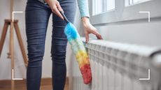 woman in blue jeans using a duster to clean a radiator to support expert comments highlighting the common radiator cleaning mistakes