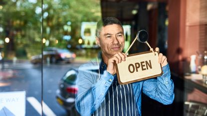 Restaurant owner holding open sign on door of business