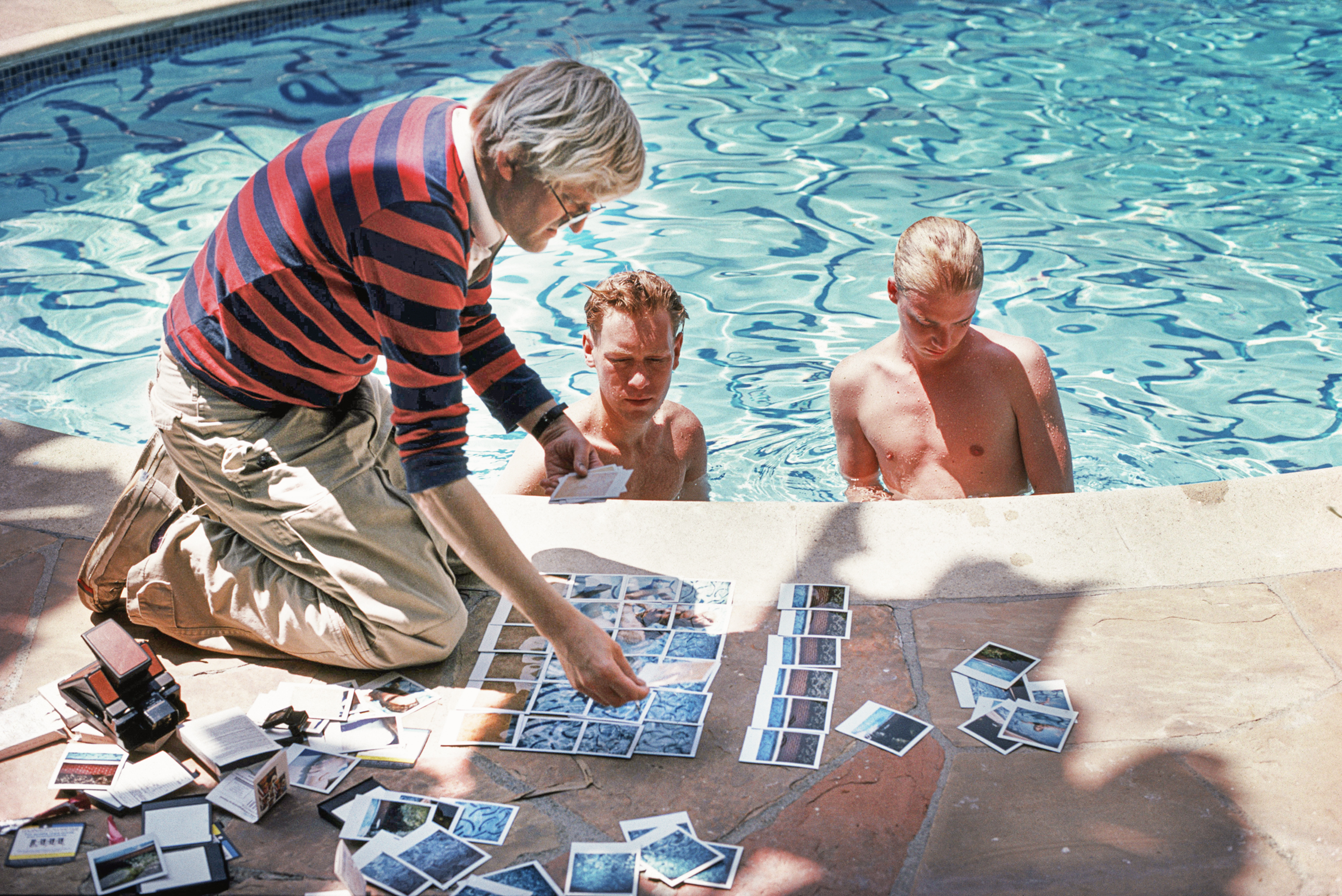 British painter, draughtsman, printmaker, stage designer and photographer David Hockney, poolside in Los Angeles, with polaroids of David Stoltz &amp; Ian Falconer, circa 1978. (Photo by Michael Childers/Corbis via Getty Images)