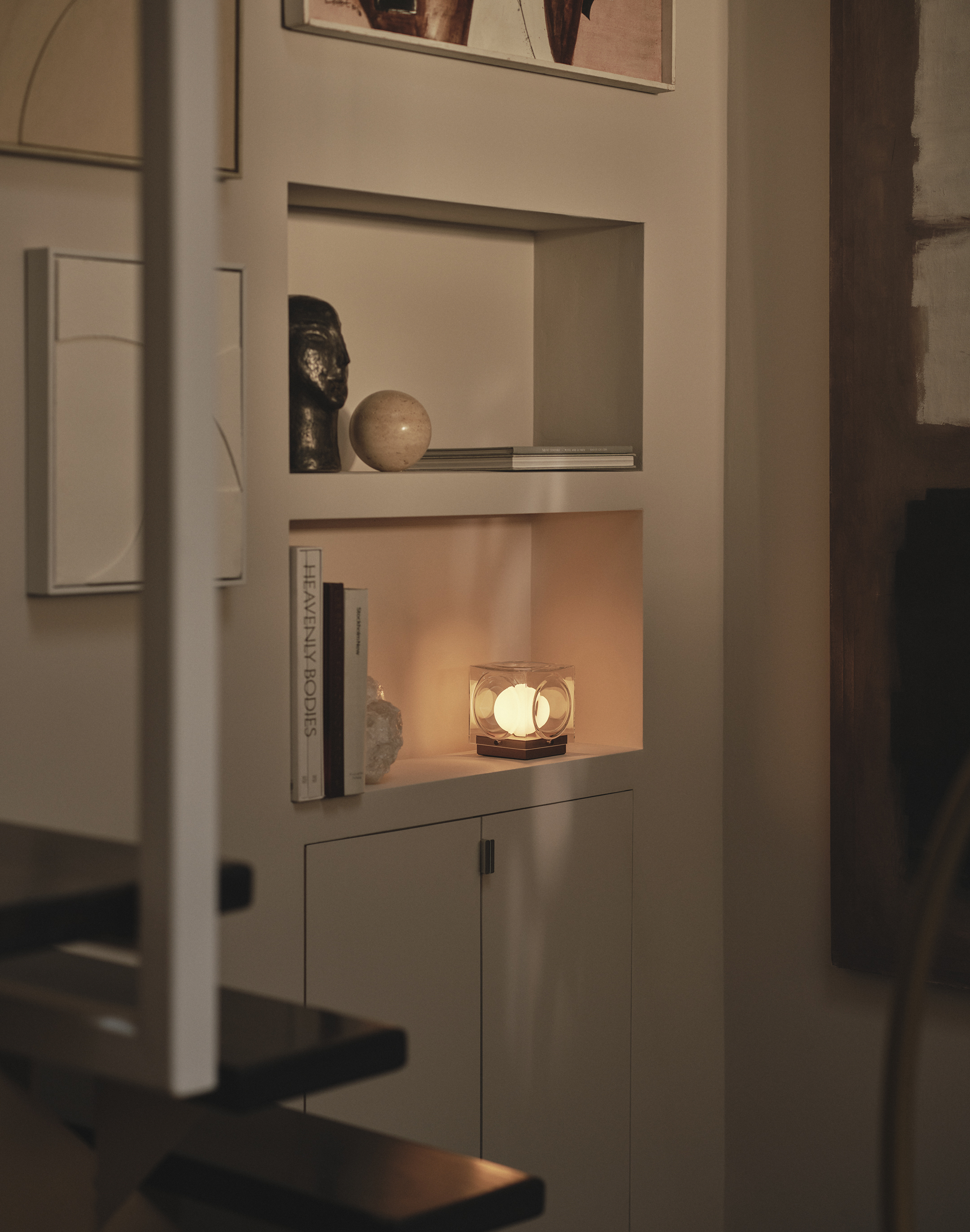 A portable lamp by Lee Broom creates a glow within a shelf beside a few books