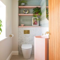 cloakroom design mistakes, small bathroom with green tiles, pink shelves, marble style tiles on lower wall and floor, brass fixtures and fittings, pink basin