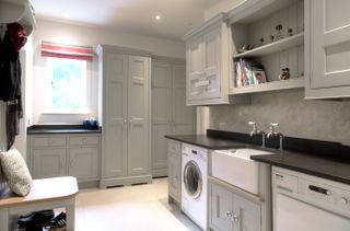 modern grey boot room within a utility space, with grey cupboards, a white butler's sink and a white washing machine