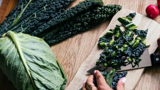 woman's hands chopping kale at wooden table