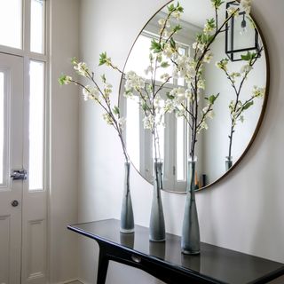 White hallway and front door with round mirror above a narrow black console table