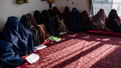 Women in Afghanistan sit together in a semi-circle with their bodies and faces covered by burkas