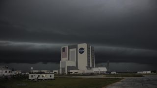 a picture of a large, square building with grey-black clouds looming overhead