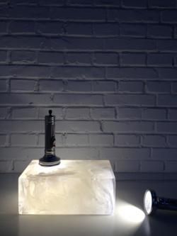 A block of marbled glass is illuminated by two torches, one standing light-down on the block, and the other on the floor pointing towards it