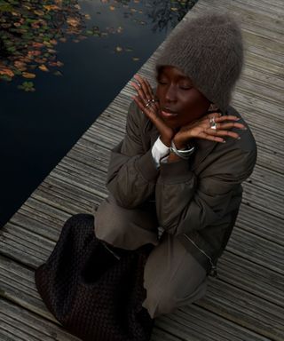 Content creator Danielle Jinadu poses in the English countryside while wearing a cozy neutral outfit.