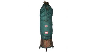 An artificial Christmas tree covered by a dark green Christmas tree storage bag on a rolling Christmas tree stand, for the best Christmas tree storage bags.