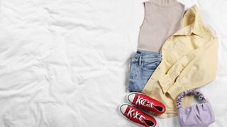 Folded clothes, shoes, and bag spread out on bed