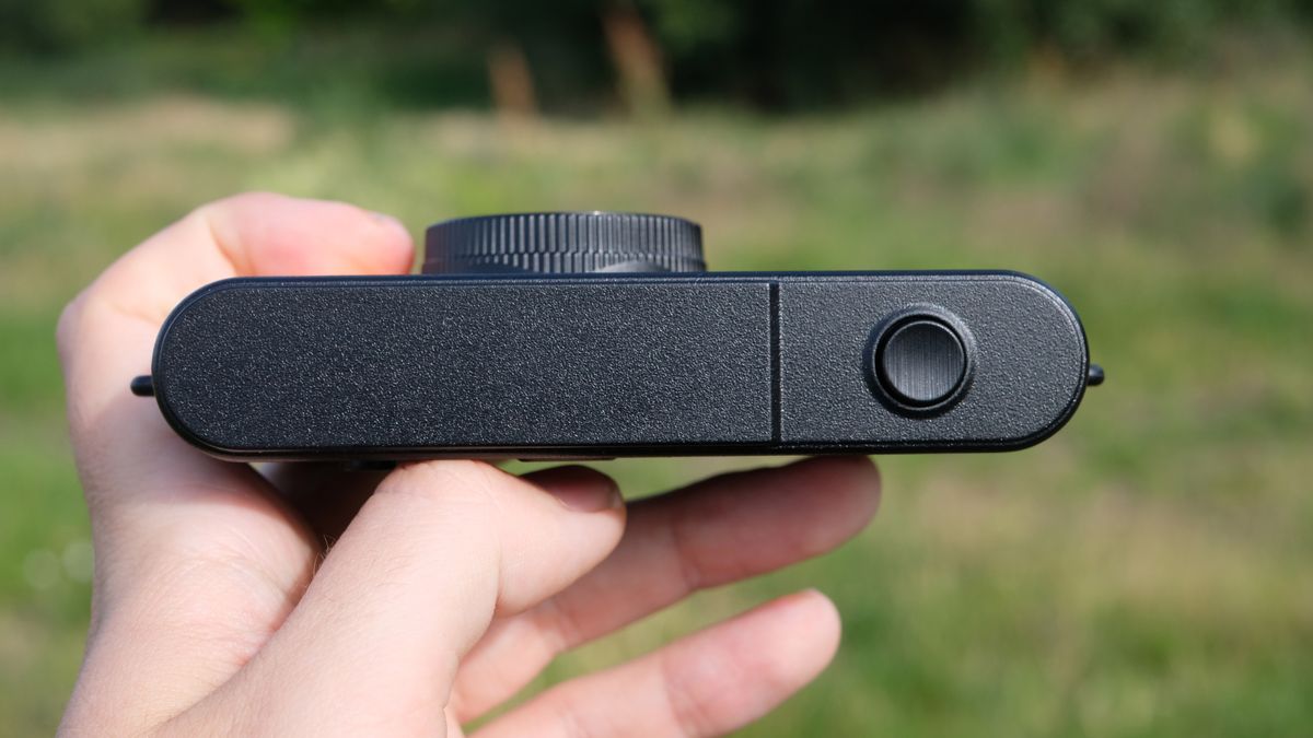 Photograph of man's hand holding Camp Snap 2 digital camera, in yellow colorway, top plate with shutter button