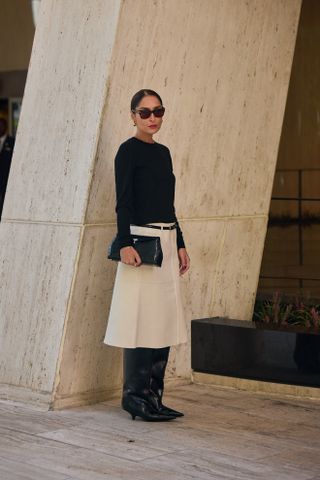 Woman wearing a white skirt, black boots, and a blue sweater in New York City.