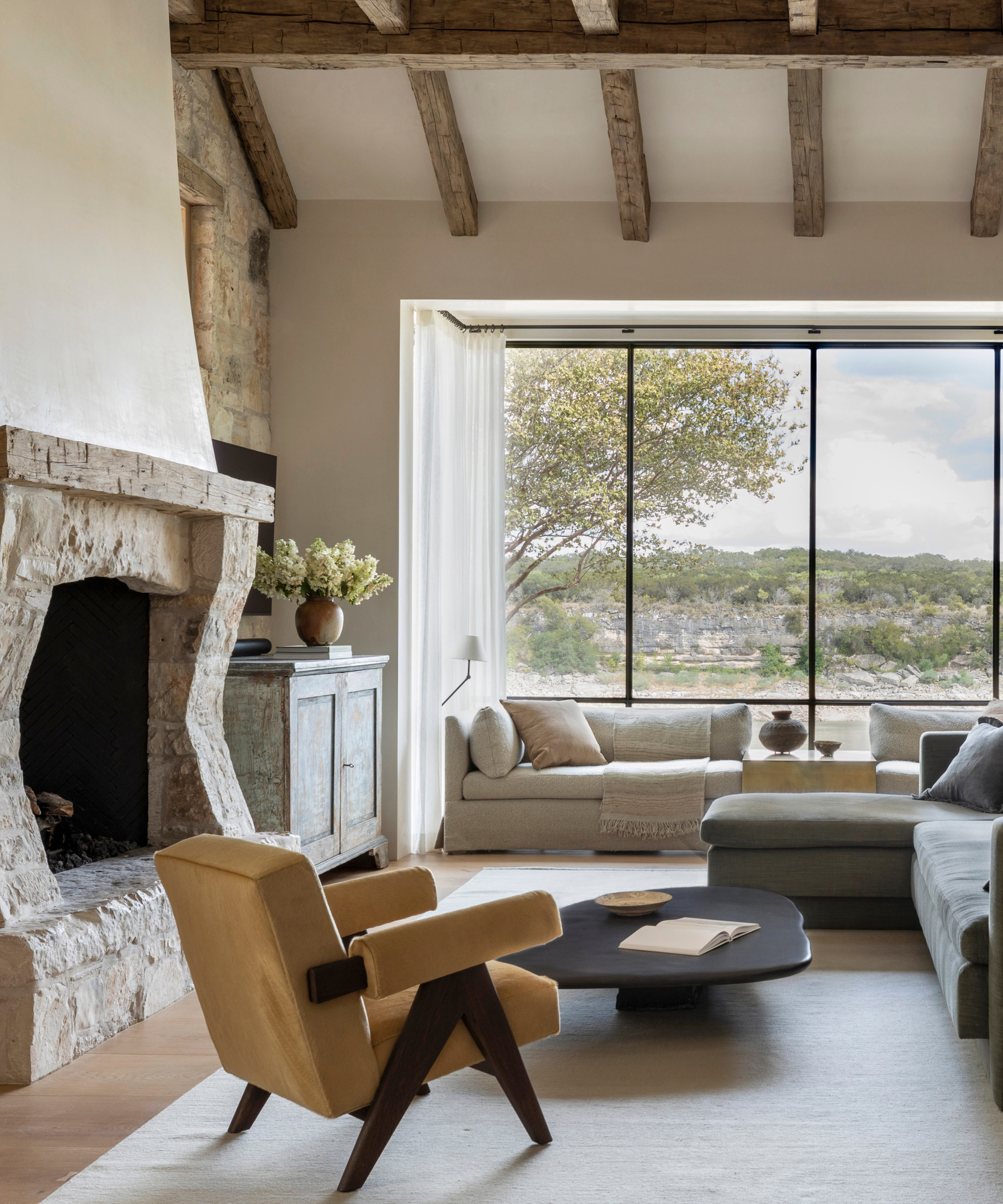 A neutral-toned living room with a large fireplace and an outdoor view