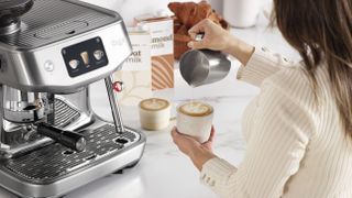 Woman pouring latte using milk steamed with Sage Oracle Jet coffee maker