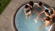 a birds eye view of a family sitting in one of the best inflatable hot tubs, in a paved area of a garden