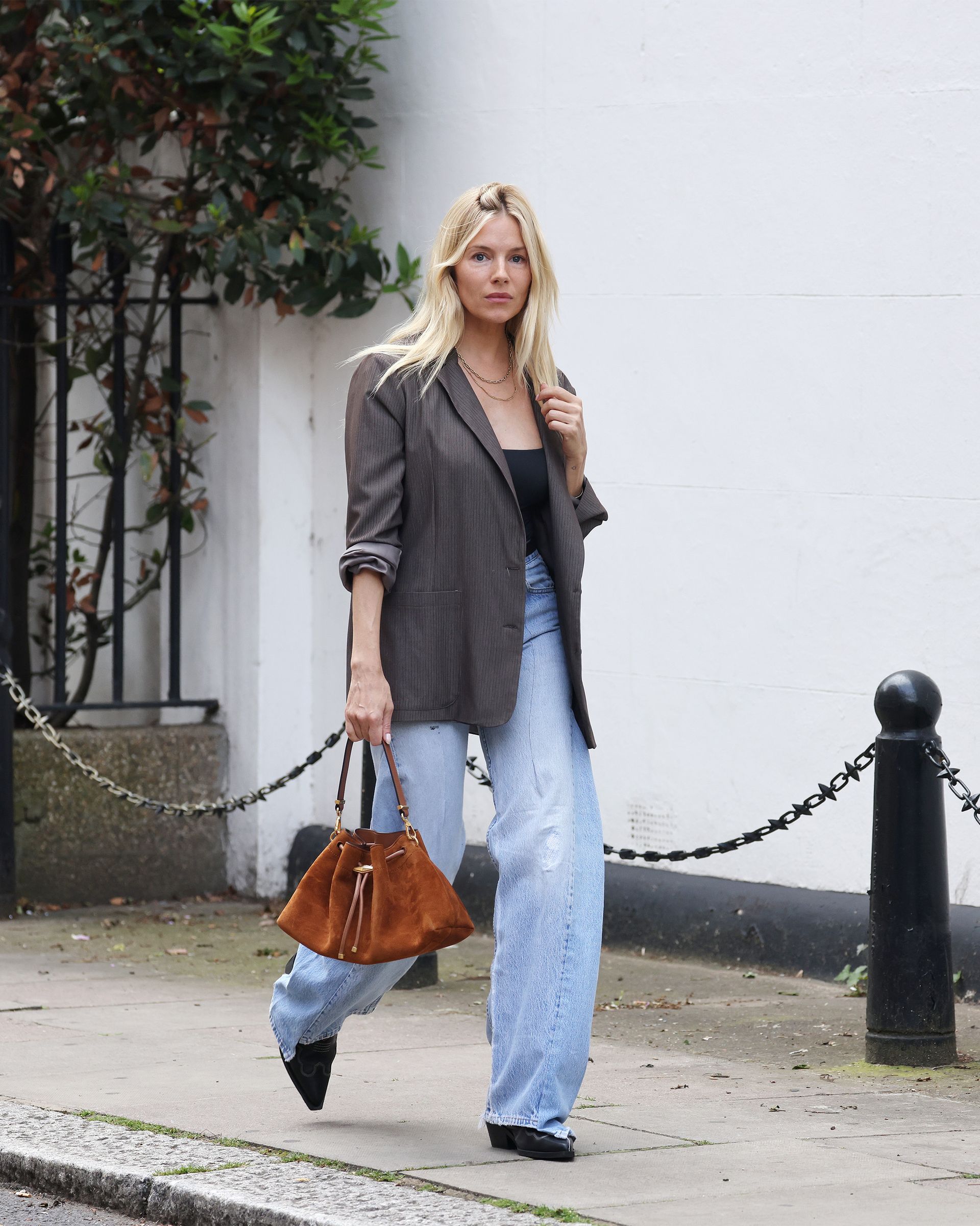 Sienna Miller wears a gray blazer with high waisted jeans.