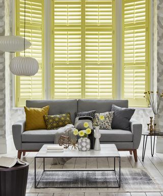 A living room with yellow shutters and a gray sofa