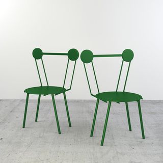 2 green metal chairs photographed in a room with white walls and grey floor