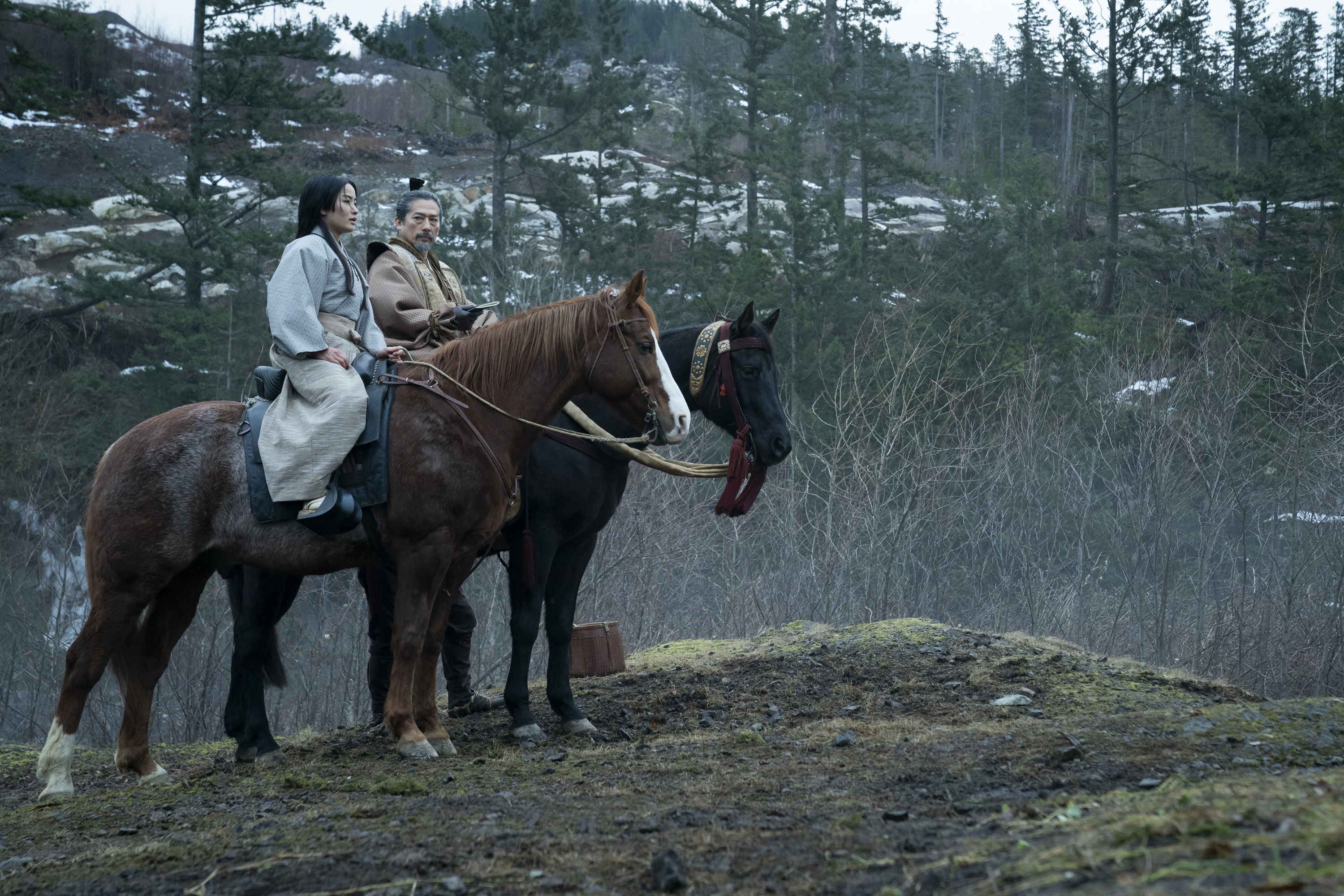 two people (anna sawai as toda mariko, hiroyuki sanada as yoshii toranga) sit on horseback in a forest, in 'shogun'