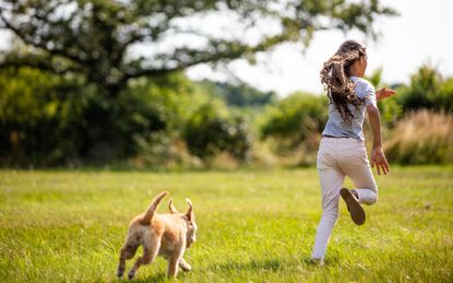 girl and dog running through a field in the countryside