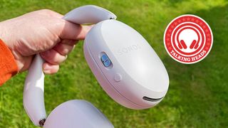Sonos Ace headphones being held up by a hand in front of a green lawn