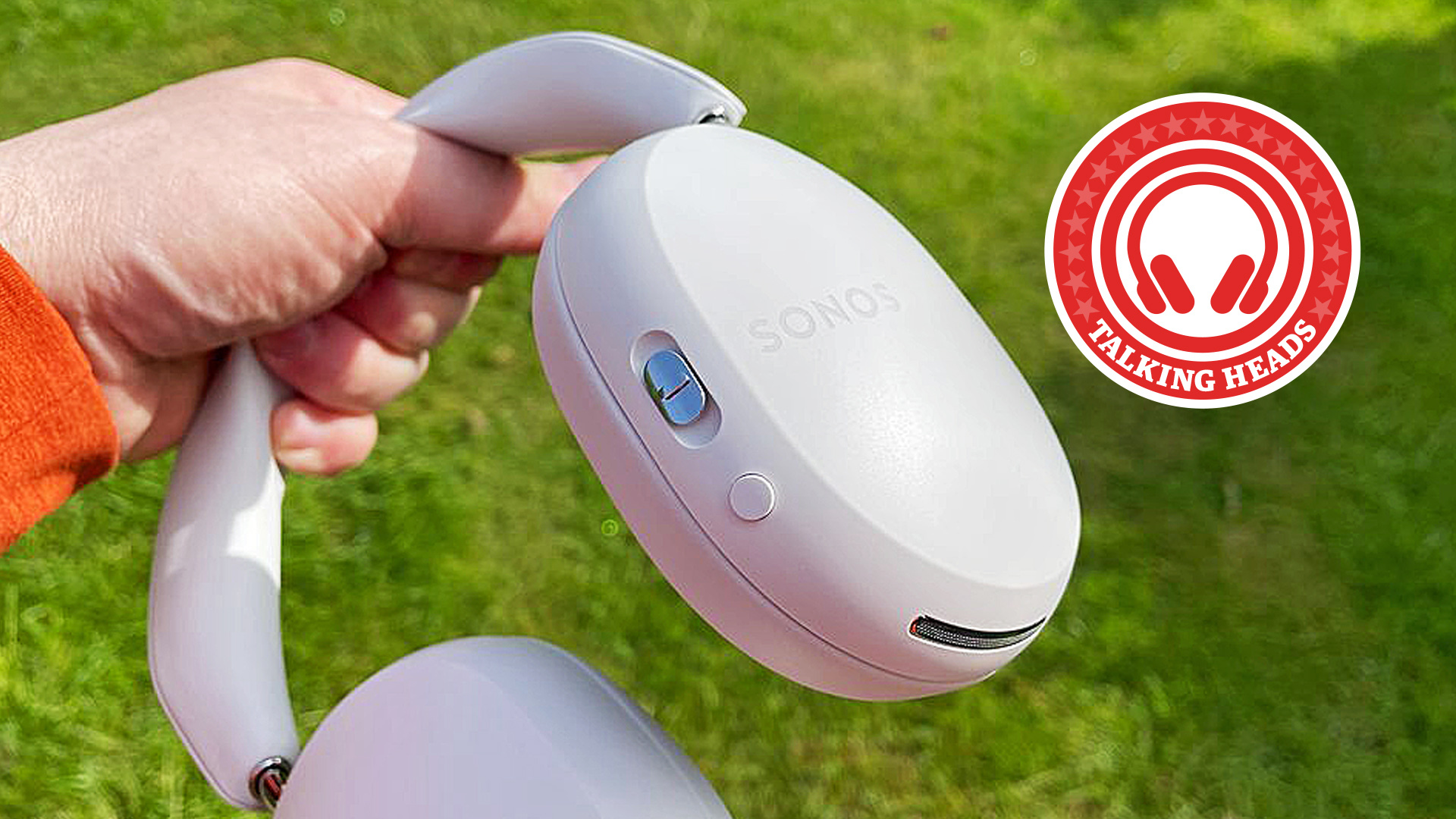 Sonos Ace headphones being held up by a hand in front of a green lawn