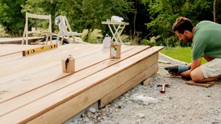 Man fixing wooden decking boards to front of decking frame