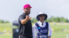 Jon Rahm gestures over to something towards the camera while standing next to Harold Varner's caddie at LIV Golf Dallas 2025