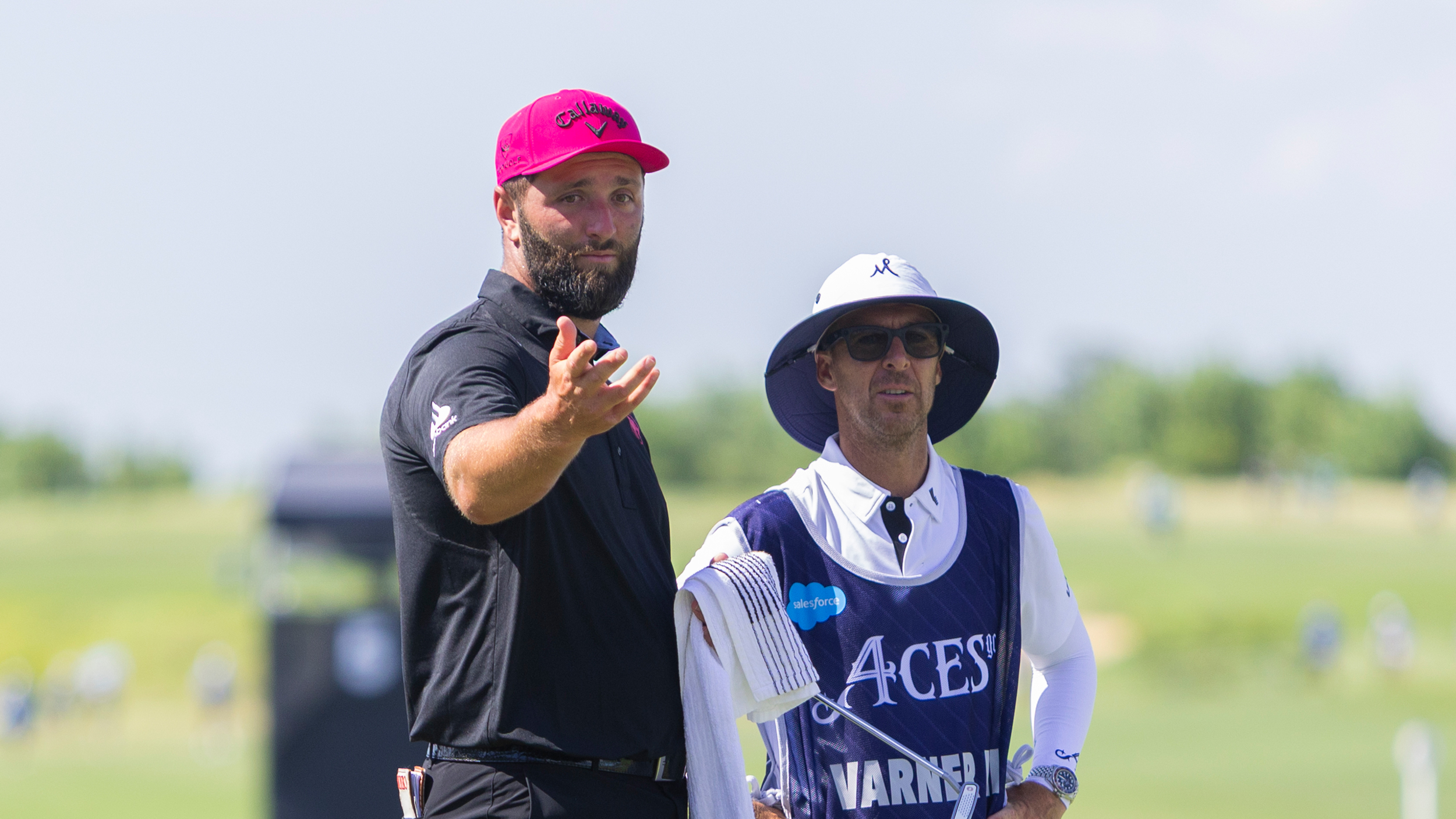 Jon Rahm gestures over to something towards the camera while standing next to Harold Varner&#039;s caddie at LIV Golf Dallas 2025