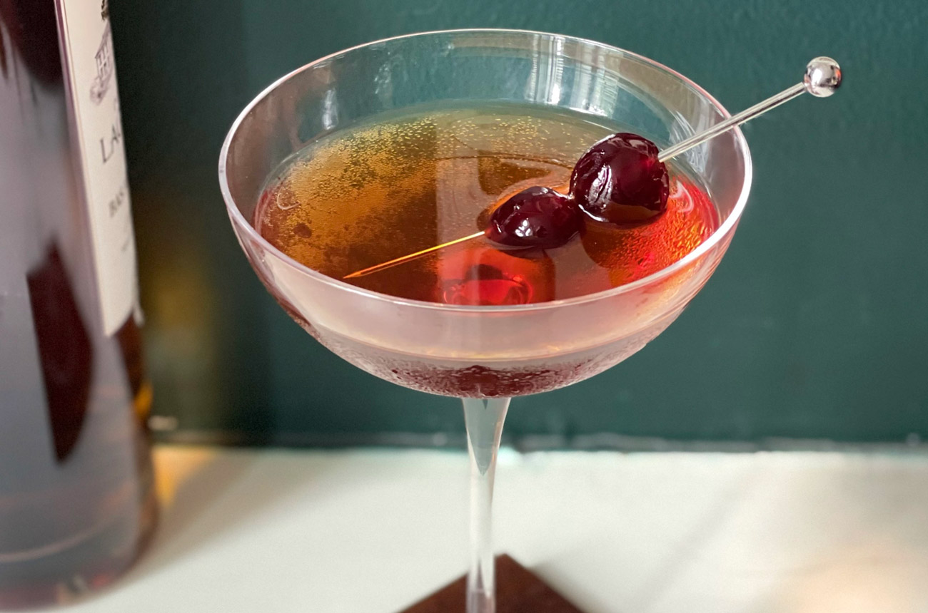 A cocktail in a glass with two cherries