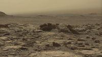 A dull yellow-tinted, rocky terrain blown with dust, as the sky in the distance matches the ground's dusty tones.