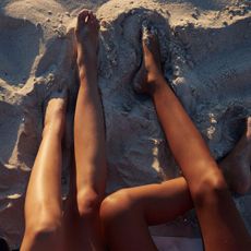 three women's tanned legs in the sand