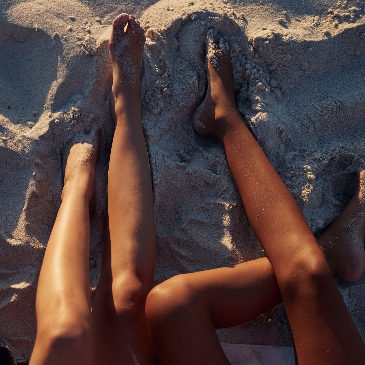 three women&#039;s tanned legs in the sand