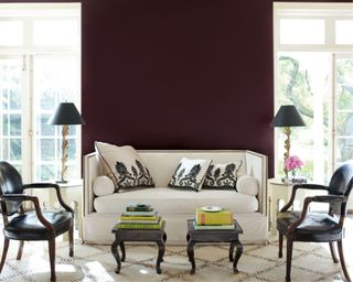 living room with a dark purple wall, balcony doors, white sofa with a neutral rug and black armchairs and tables