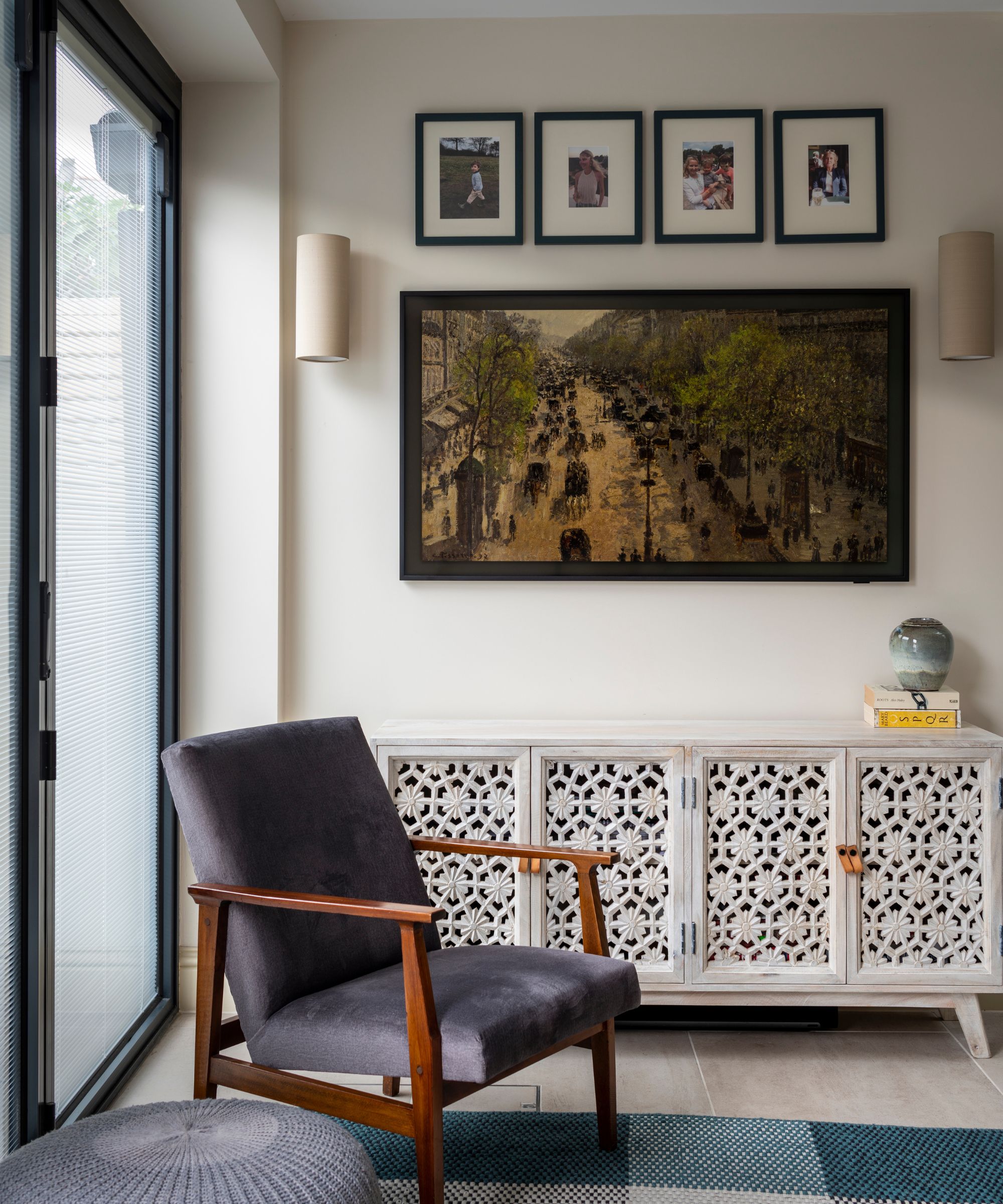 Living room with prints hung on wall, wood carved console, midcentury chair and pouf