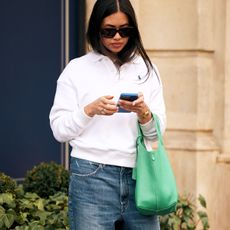 Woman in a white polo sweatshirt and jeans looking at a phone