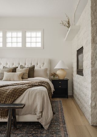 A bedroom with white walls, small glass brick windows, a large rug, and a stone wall