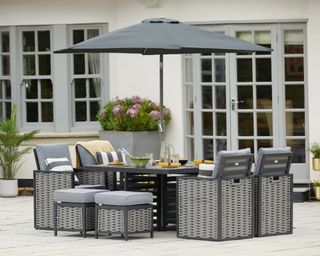 A grey rattan dining set with a parasol on a paved patio courtyard