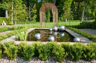 garden pond ideas: metal sculptures in pond with arch in background