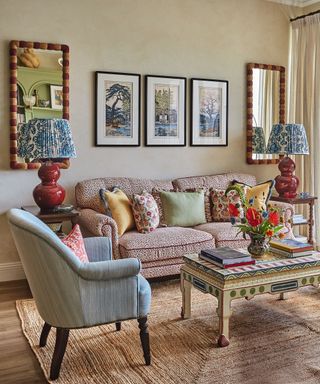 living room with patterned sofa and armchair and textured seagrass rug and colourgul painted wooden coffe table and art on walls behind with symmetrical mirrors