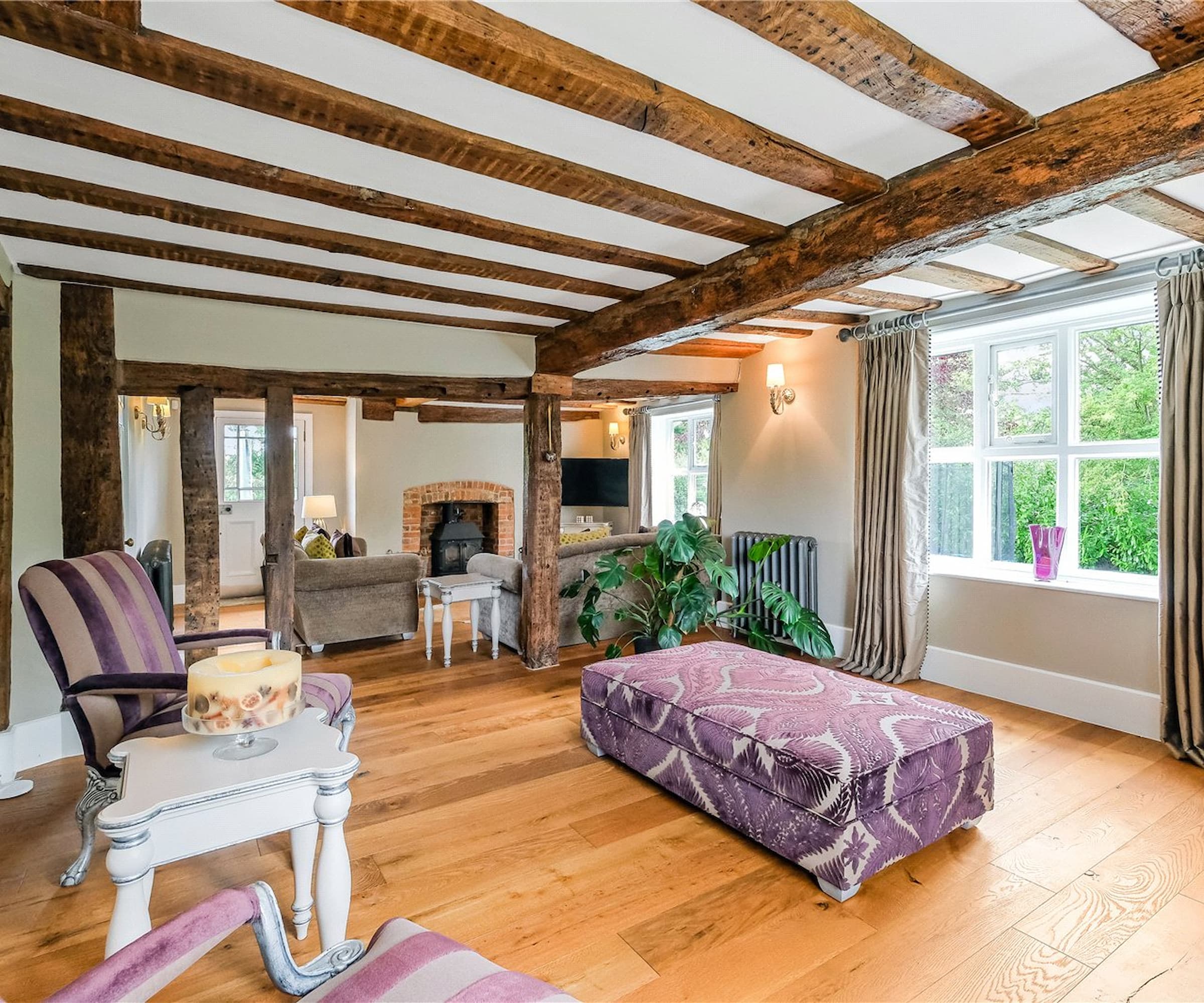 An old fashioned living room with overhead wooden beams and wooden flooring and a brick fireplace