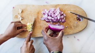 Hands chopping garlic and red onions on thick wooden chopping board