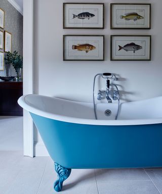 A blue free standing bath with four pictures on the wall above