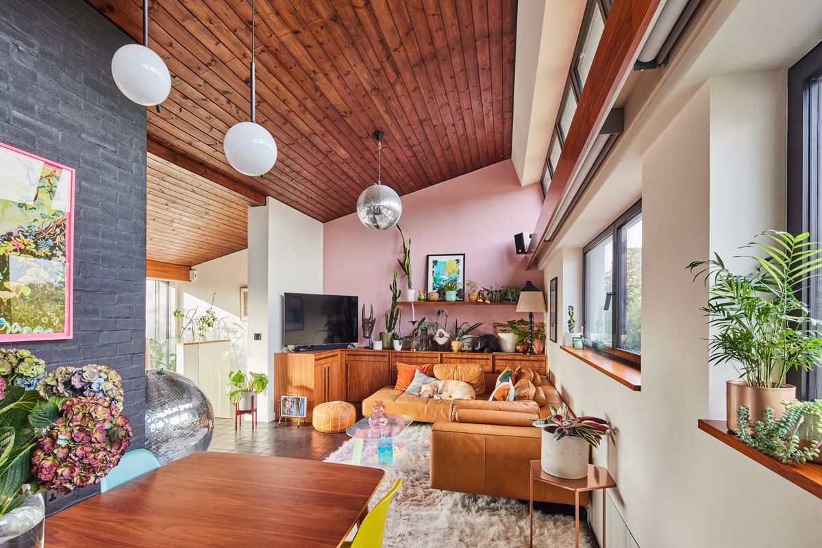 The interior of a modernist home with a pink feature wall, an l-shaped leather sofa with a sleeping golden retriever, and a large disco ball 